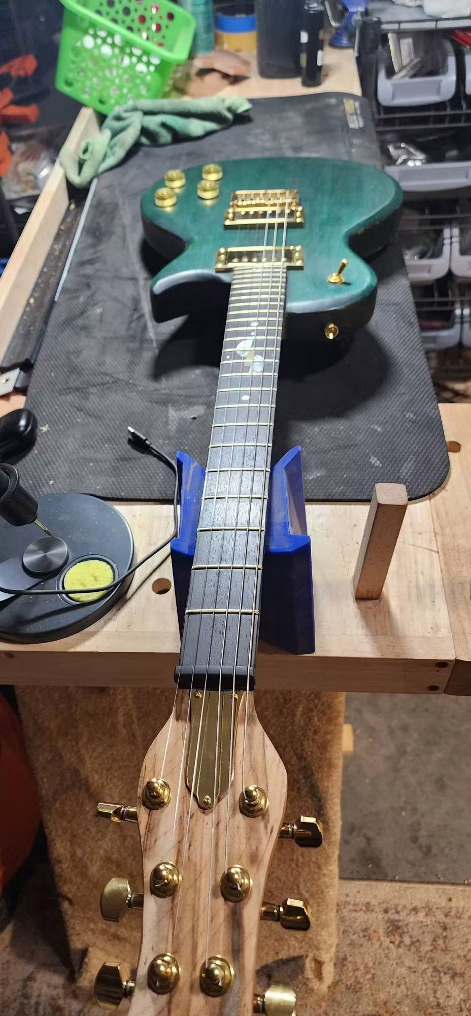 Green guitar with gold hardware and fretboard inlays on the workbench